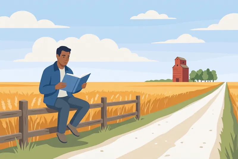 A man reads a book sitting on a fence beside a gravel road through wheat fields, with a red grain elevator in the distance.